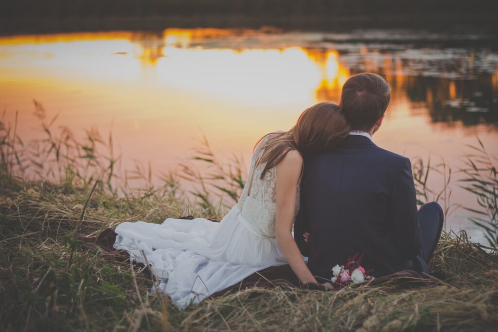 A couple sitting on the grass in front of a lake